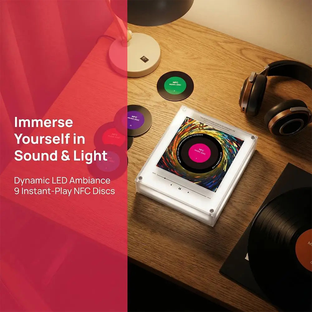 White acrylic NFC music player with a colorful vinyl disc, headphones, and additional NFC discs on a wooden desk.