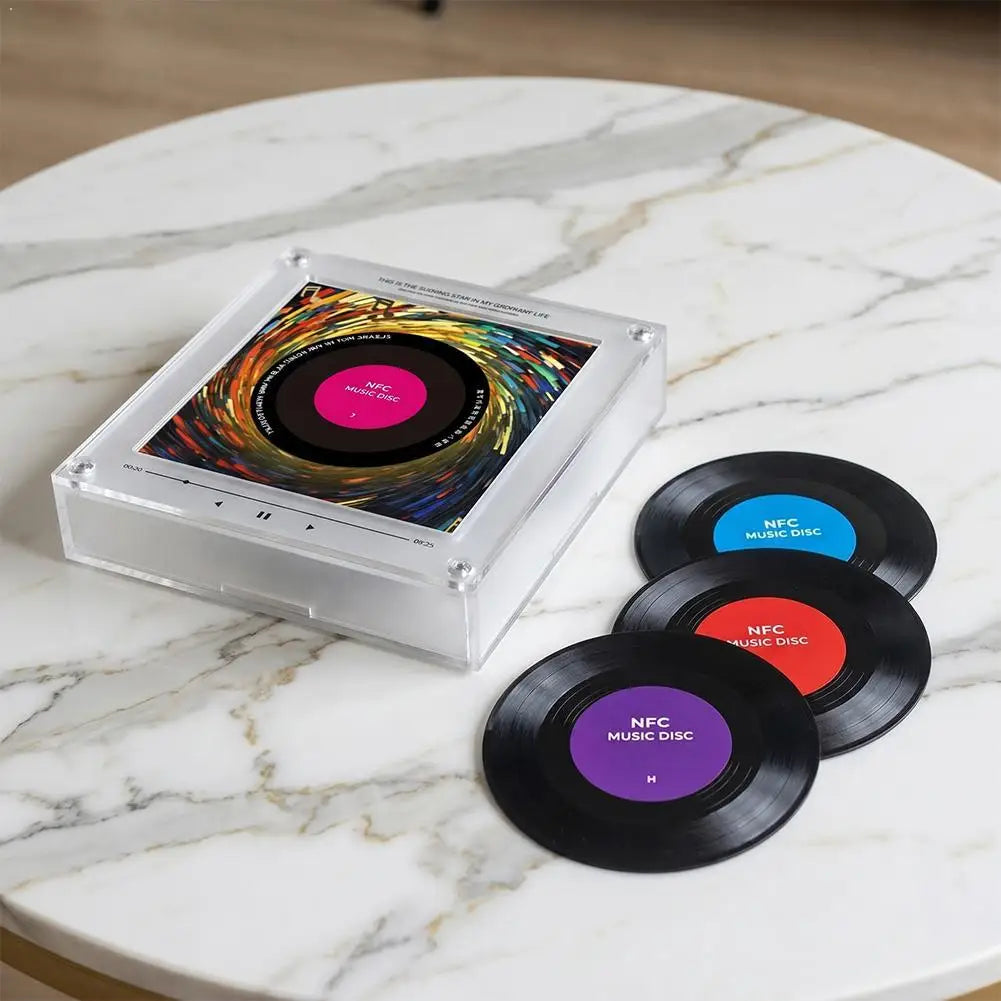 Clear acrylic NFC music player with a colorful vinyl disc display and three black NFC music discs on a marble table.